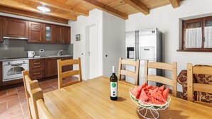 Een keuken met houten kastjes, een eettafel met stoelen, een koelkast en een fles wijn.