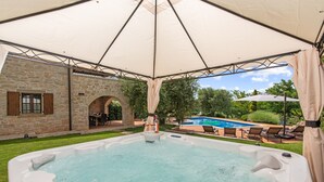 Een bubbelbad onder een luifel, met een stenen gebouw en een zwembad op de achtergrond.