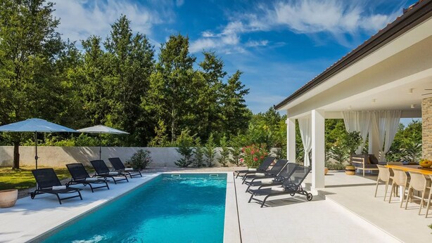 A swimming pool with lounge chairs and umbrellas, surrounded by greenery and a covered patio area. - Magdalena in Labin With 5 Bedrooms and 5 Bathrooms (Labin)