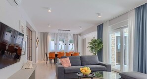 Un salon moderne avec un canapé gris, une table basse en verre et un coin repas comprenant des chaises orange et une table blanche.