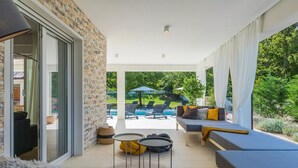 A covered outdoor area with a stone wall, a sofa with cushions, a small table, and a pool in the background. - Magdalena in Labin With 5 Bedrooms and 5 Bathrooms (Labin)