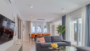 A modern living room with a grey sofa, a glass coffee table, and a dining area with orange chairs and a white table. - Magdalena in Labin With 5 Bedrooms and 5 Bathrooms (Labin)