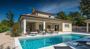 Une maison moderne dotée d’une piscine, d’un espace salon extérieur et d’une façade en pierre.