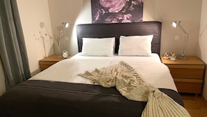 A neatly made bed with a dark headboard, white pillows, and a knitted throw. There are two bedside tables with lamps and a clock on one. A floral artwork is above the bed. - Kvarta in Barban With 3 Bedrooms and 3 Bathrooms (Barban)
