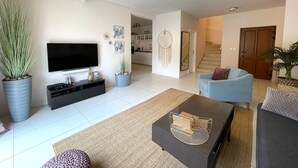 A modern living room with a flat-screen TV, a coffee table, and a sofa. There is a staircase leading to an upper floor, and a kitchen area is visible in the background. - Kvarta in Barban With 3 Bedrooms and 3 Bathrooms (Barban)