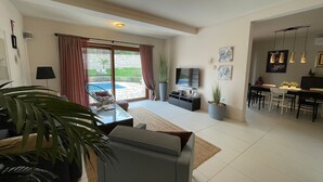 A spacious living area with a sofa, coffee table, and a dining table with chairs. There is a TV, a potted plant, and a sliding glass door leading to a patio. - Kvarta in Barban With 3 Bedrooms and 3 Bathrooms (Barban)