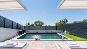 Un área de piscina moderna al aire libre con sillones reclinables, un tobogán y un cielo despejado.