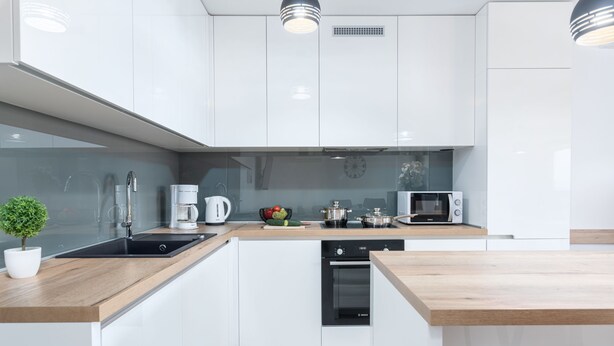 Una cocina moderna con armarios blancos, encimera de madera, lavavajillas Bosch, microondas y cafetera.