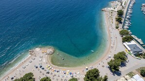 Vista aérea de una playa con aguas cristalinas, una hilera de sombrillas y un puerto deportivo con barcos.