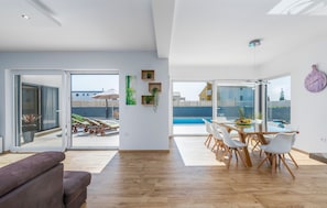 A spacious living area with a wooden floor, a dining table with white chairs, and a view of a swimming pool through large glass doors. - OL JU in Pula With 3 Bedrooms and 1 Bathrooms (Pula)