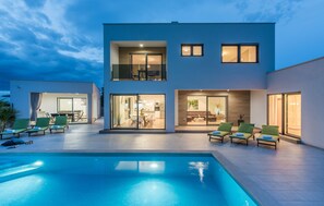 Ein modernes, zweistöckiges Haus mit Swimmingpool, Sitzgelegenheiten im Freien und einem gut beleuchteten Innenraum.