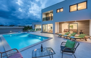 A modern poolside area with a swimming pool, lounge chairs, and a table with a bottle and glasses. - OL JU in Pula With 3 Bedrooms and 1 Bathrooms (Pula)