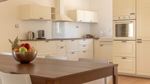 A modern kitchen with white cabinetry, a wooden dining table, and a fruit bowl. - Milla Hvar in Rudina Hvar (Stari Grad)