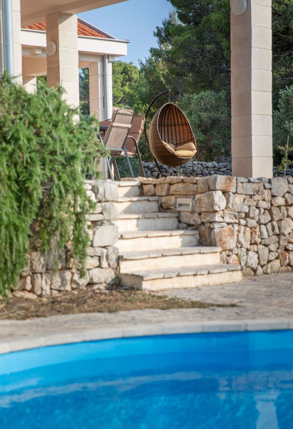 Área de piscina com degraus de pedra que levam a um espaço de descanso com duas cadeiras de vime.