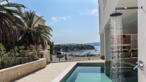 Ein Pool auf dem Dach mit Wasserfall, umgeben von Palmen und Blick auf das Meer.