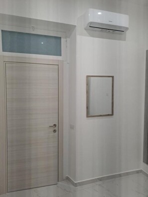 A room with a wooden door, an air conditioning unit mounted on the wall, and a framed picture. - Giorgia's House (Campofelice di Roccella)
