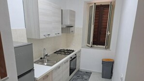 A compact kitchen with white cabinets, a gas stove, a sink, and a window with brown shutters. - Giorgia's House (Campofelice di Roccella)