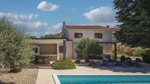 Ein modernes, zweistöckiges Haus mit Swimmingpool, Sitzgelegenheiten im Freien und einem Garten.