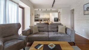 Ein modernes Wohnzimmer mit einem grauen Sofa, einem Holztisch und einer Küche im Hintergrund.