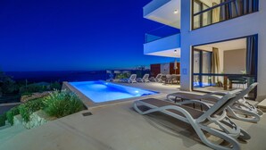 A modern outdoor pool area with lounge chairs, a clear view of the sea, and a two-story building with large windows. - Bellevue in Bast Ba ka Voda (Baska Voda)