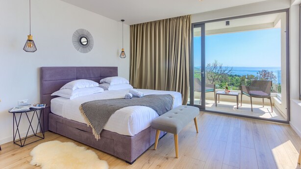 Un dormitorio con una cama grande, un banco, una mesita y vistas al exterior.