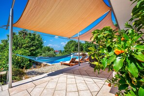 Zona de piscina con sillones de descanso y una hamaca bajo una vela de sombra.