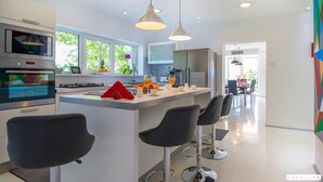 A modern kitchen with a central island, bar stools, and a dining area in the background. - Organic Gardens in Crikvenica (Crikvenica)
