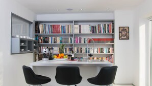 A modern kitchen with a white island, black bar stools, and a bookshelf filled with books. - Organic Gardens in Crikvenica (Crikvenica)