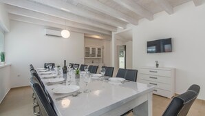 A dining area with a long table set for six, a television mounted on the wall, and a white cabinet with drawers. - Complex Kamenjak in Premantura (Medulin)