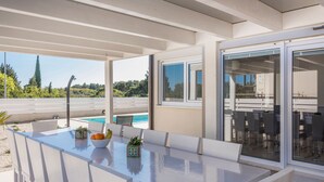 A modern outdoor dining area with a pool view, white furniture, and a clear sky. - Complex Kamenjak in Premantura (Medulin)
