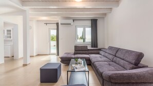 A modern living room with a sectional sofa, a glass coffee table, and a view of the outdoors. - Complex Kamenjak in Premantura (Medulin)