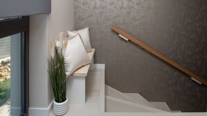 A staircase with a wooden handrail, a white wall with a leaf pattern, and a potted plant with tall green leaves. - Four Seasons Vrsi in Vrsi (Vrsi)