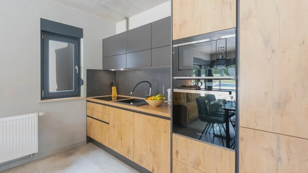 Una cocina moderna con armarios grises, encimera de madera y horno empotrado.