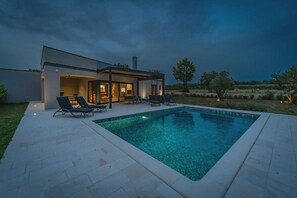 Ein modernes Haus mit Swimmingpool, Sitzgelegenheiten im Freien und einer überdachten Terrasse.