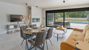 Un comedor moderno con una mesa redonda dispuesta para cuatro personas, rodeada de sillas de cuero. Un televisor de pantalla plana está montado en la pared sobre la mesa.