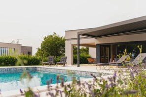 Ein moderner Poolbereich im Freien mit Liegestühlen und einer überdachten Sitzgelegenheit.
