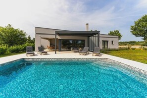 Ein modernes Haus mit Swimmingpool, Sitzgelegenheiten im Freien und einer überdachten Terrasse.