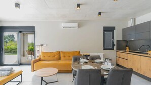 Una cocina moderna con encimera de madera y armarios negros, un comedor con mesa redonda y sillas, y un sofá amarillo.