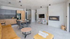 Un espacio habitable moderno con sofá, mesa de comedor, sillas, una pequeña mesa redonda, televisor y chimenea.