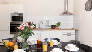 Una cocina moderna con armarios blancos, una campana extractora de acero inoxidable y un microondas. Hay una mesa de comedor con platos, vasos y un jarrón de flores.