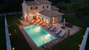 Una casa de dos plantas con piscina, zona de estar exterior y terraza cubierta.