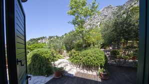 A wooden deck with potted plants, a stone wall, and a view of a mountainous landscape. - Makar in Makarska With 2 Bedrooms and 1 Bathrooms (Makarska)