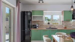 A modern kitchen with green cabinets, a black refrigerator, a microwave, and a dining area with a glass table and chairs.