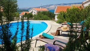 A pool area with lounge chairs, a wicker chair, and a view of the sea and mountains. - Susanna Hvar in Rudina Hvar (Stari Grad)