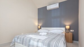 Een net opgemaakt bed met een gestreept deken, twee nachtlampjes en een wandairconditioner.