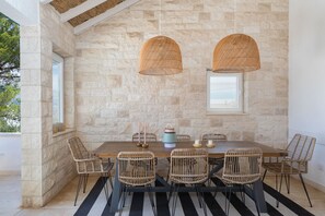 Un coin repas agrémenté d’un mur en pierre, de chaises en osier, d’une table en bois et de lampes en osier suspendues.