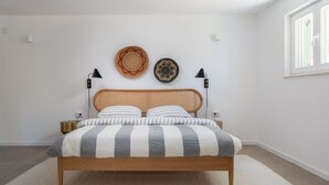 Une chambre à coucher avec un lit en bois, une literie à rayures, deux lampes fixées au mur et deux décorations murales tissées.