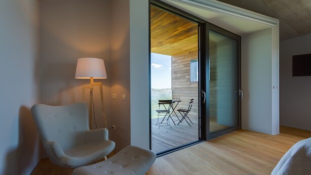A modern room with a sliding glass door leading to an outdoor deck, a cushioned chair, a small table, and a floor lamp. - Vista in Zamask With 3 Bedrooms and 3 Bathrooms (Pazin)