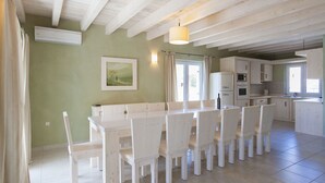 A spacious kitchen with a dining area, featuring a long table and chairs, a hanging light fixture, and a window with curtains. - Bianca Pula in Pula With 8 Bedrooms and 4 Bathrooms (Medulin)