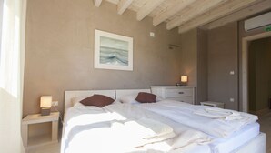 A hotel room with a large bed, a bedside table with a lamp, a painting on the wall, and a door with an exit sign. - Bianca Pula in Pula With 8 Bedrooms and 4 Bathrooms (Medulin)